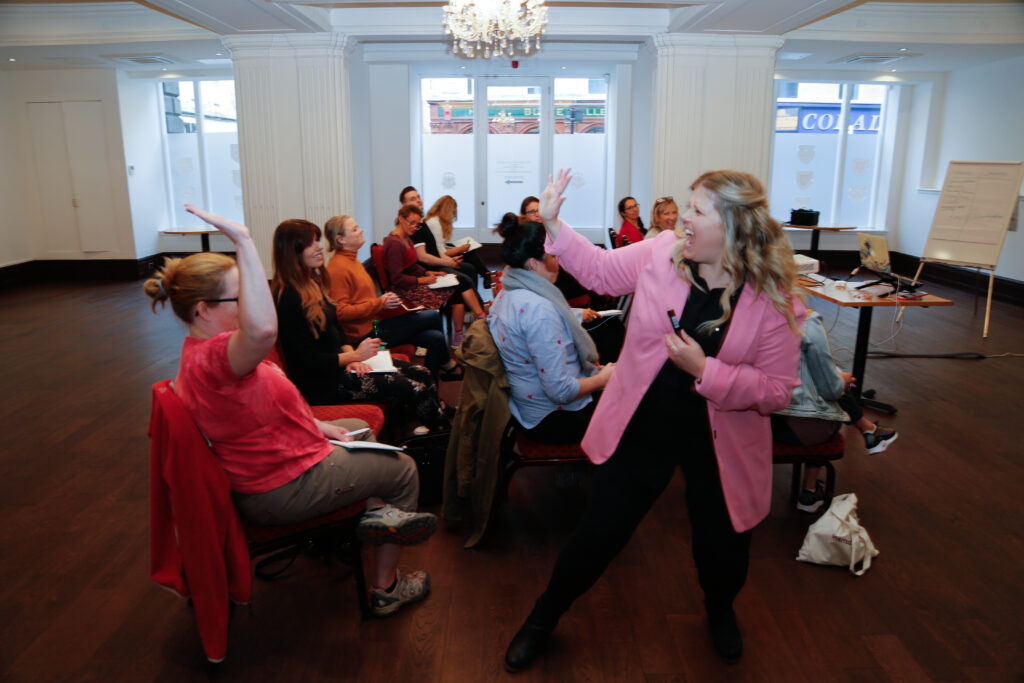 Sooz Young delivering an interactive Technology Coaching workshop, high-fiving a participant while leading a group session on digital skills and business growth. Known for her fun, engaging, and empowering style, Sooz helps small business owners build confidence with the Digital Mindset Tekunoji Method